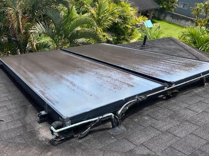 Solar panels installed on a residential roof surrounded by tropical greenery.